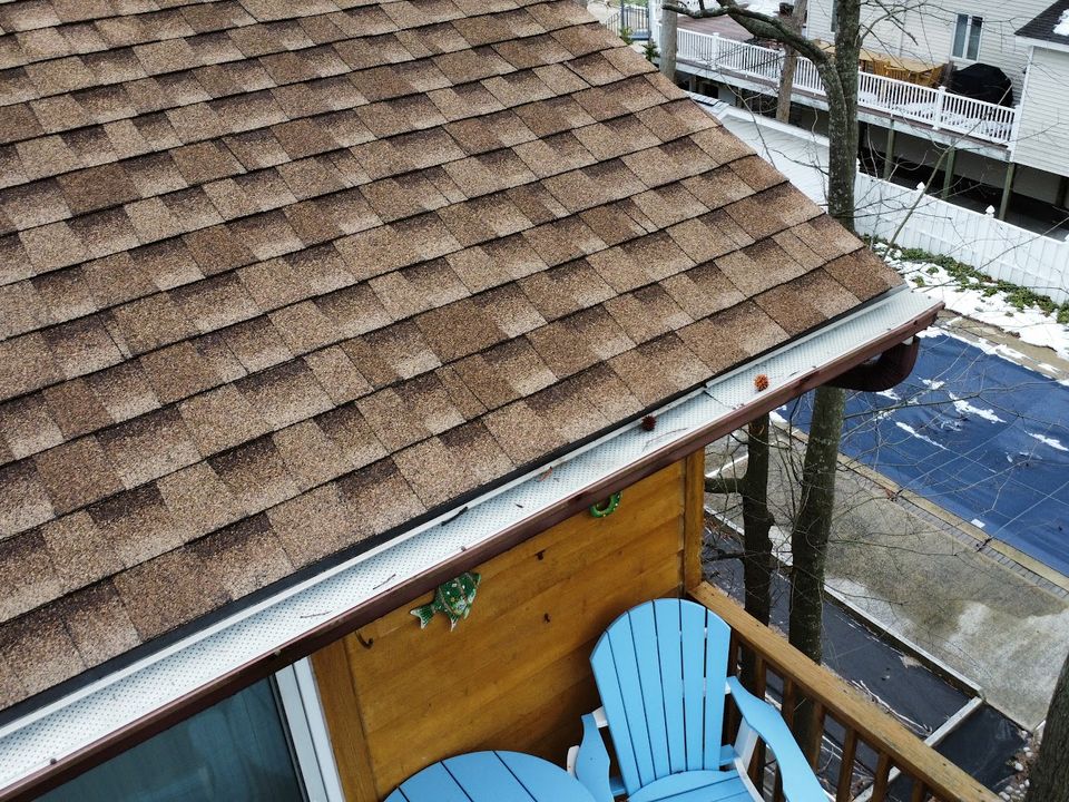 Drone view looking down a shingled roof edge and gutter above a deck with blue chairs